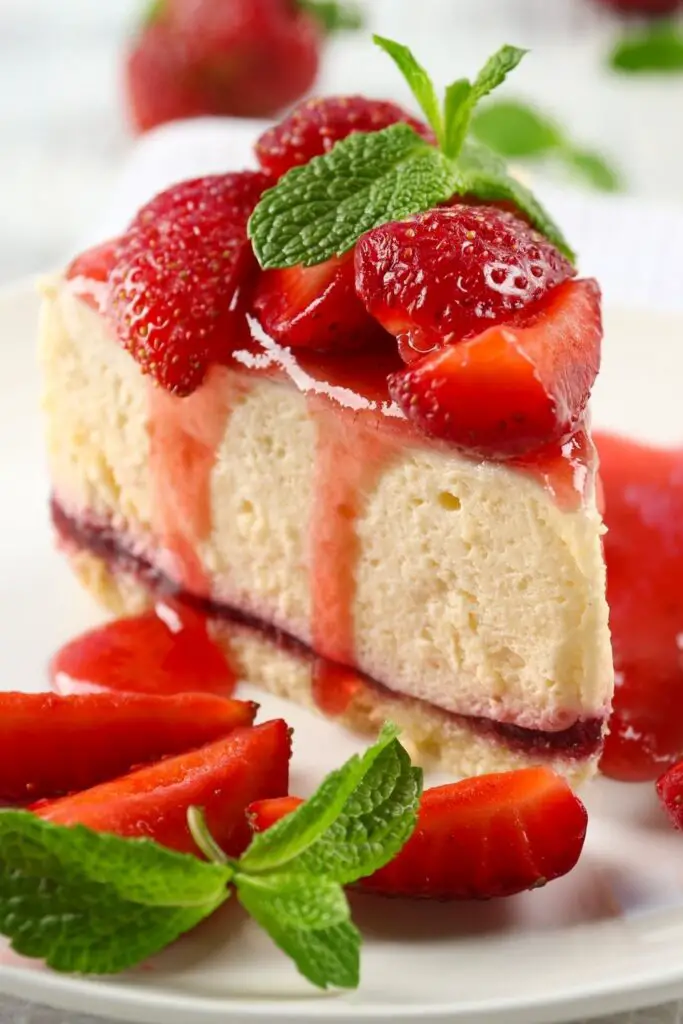 Le 30 migliori ricette di cheesecake per il dessert più goloso. La foto mostra una cheesecake dolce alle fragole con salsa di fragole servita su un piatto con una foglia di menta sopra.
