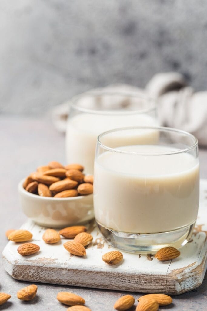 Mandelmjölk i ett glas bredvid mandel i en liten skål