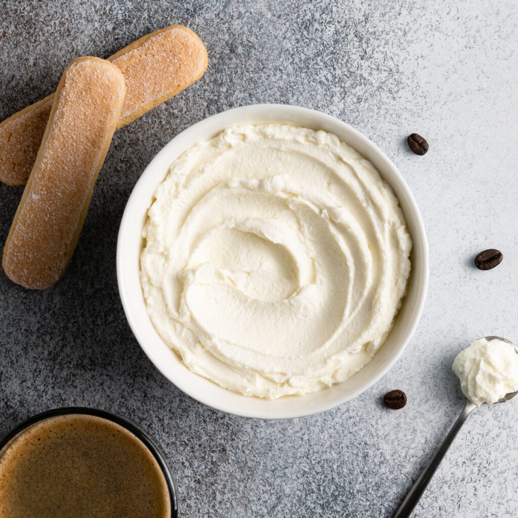 Crema batida en un tazón blanco con Lady Fingers y café al costado