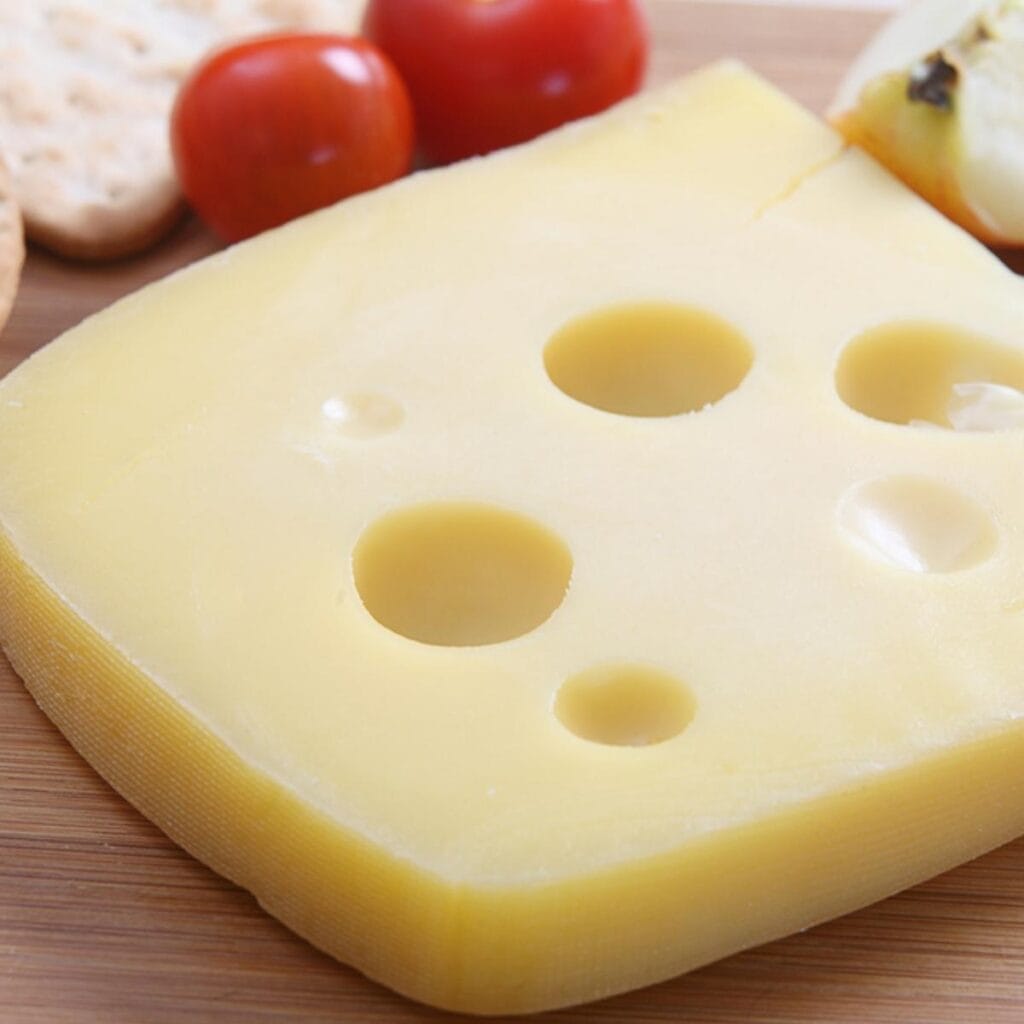 Queso Jarlsberg en lonchas encima de una mesa de madera