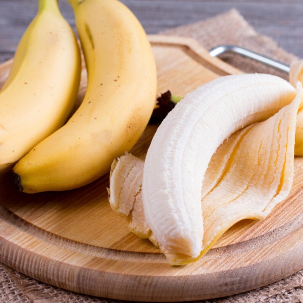 Kuoritut ja kuorimattomat banaanit puisella leikkuulaudalla