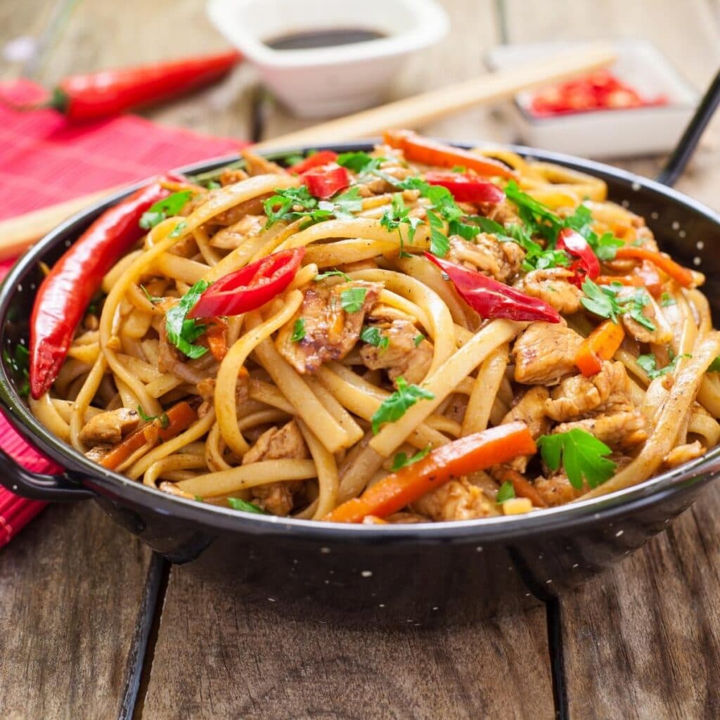 Chow Mein en una sartén cubierto con verduras y carne de pollo