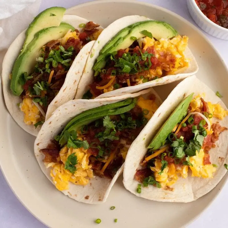 Mic dejun Tacos cu felii de avocado, bacon și ouă garnisite cu ceapă verde și coriandru