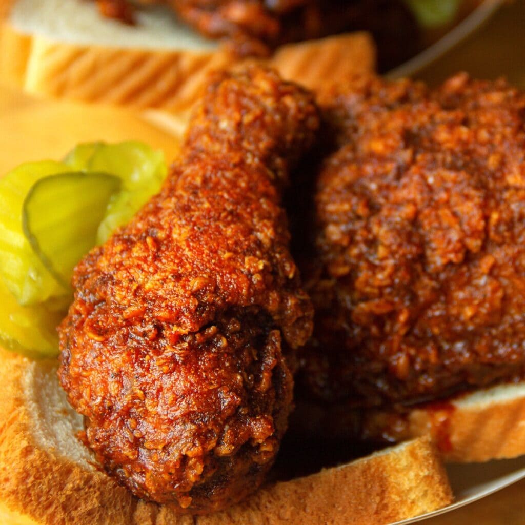 Hot Nashville Chicken disajikan di atas irisan roti putih yang diberi acar