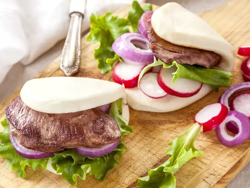 Fusion Gua Bao (በእንፋሎት የተሰራ ዳቦ ሳንድዊች) በመቁረጫ ሰሌዳ ላይ