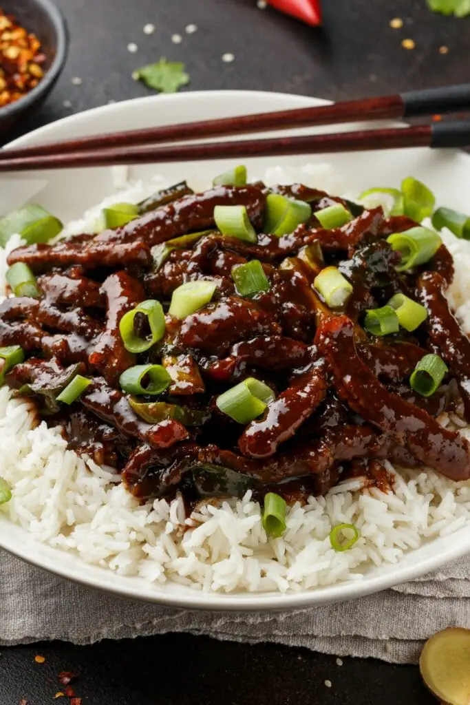 Tuisgemaakte Mongoolse beesvleis met rys en groen uie op 'n wit bord
