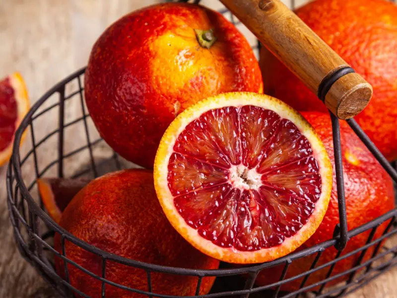 Naranjas sanguinas enteras y cortadas en una cesta de metal