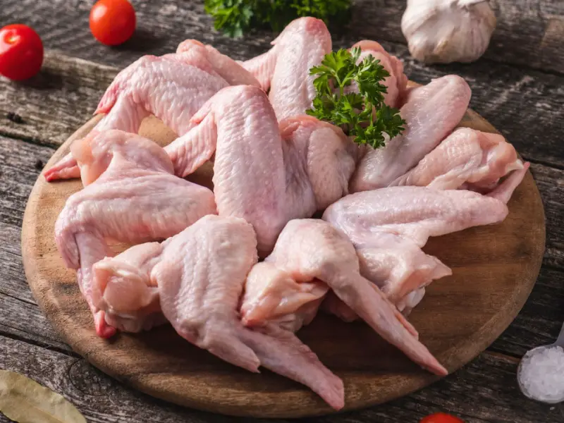 Frësch réi Pouletflügel op engem ronnen Schneidebrett