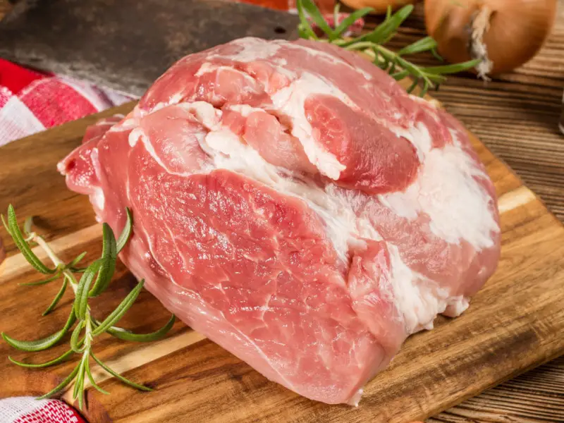 Paletilla de cerdo cruda con romero en una tabla para cortar