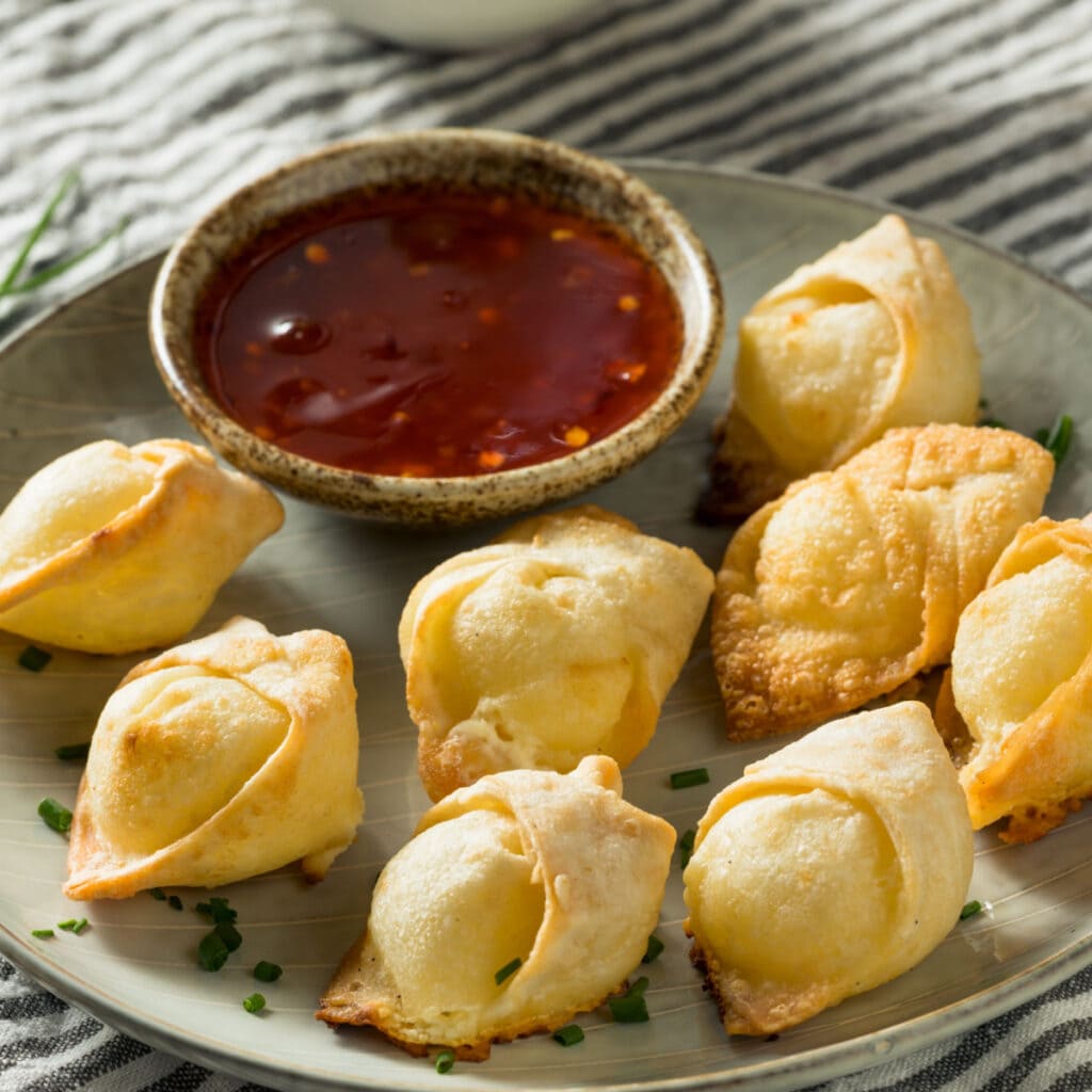 Crispy cream cheese wontons on a plate with dipping sauce