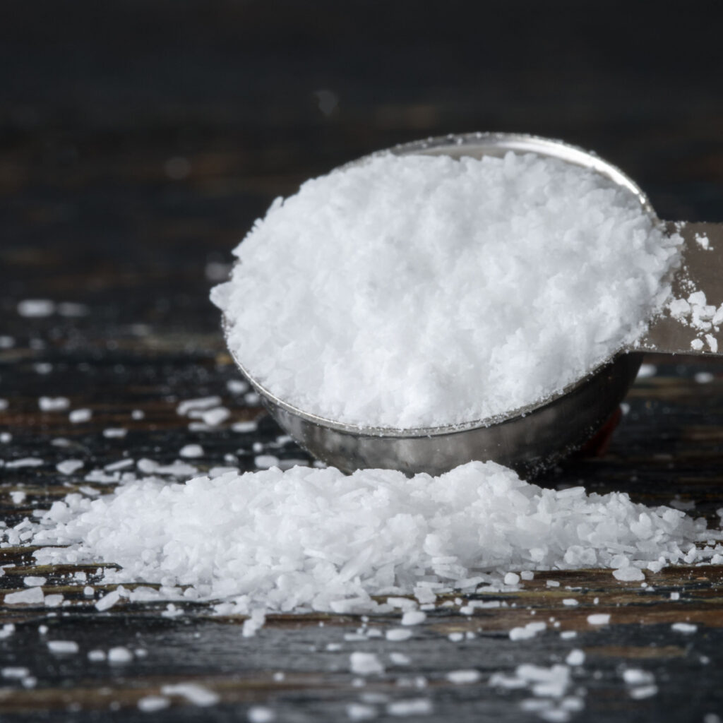 Rozlana sól w łyżeczce na drewnianym stole: sól koszerna i sól morska: jaka jest różnica?