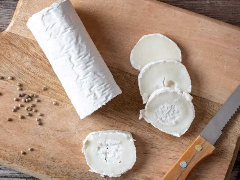 Queso de cabra entero y en rodajas sobre una tabla de cortar de madera