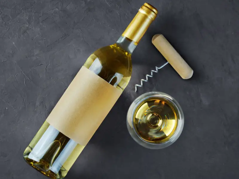 Botella de vino sobre una mesa de hormigón con abridor de vidrio y corcho