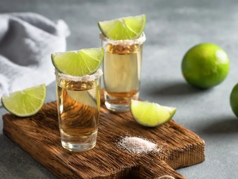 Tequila Joven en un vaso de chupito con limón y sal rosa sobre una tabla de madera